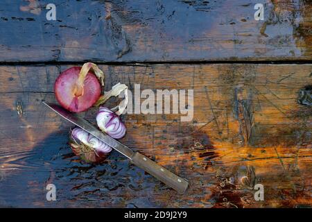 Purple Crimean onion on a wooden surface. Two bulbs in husk, one cut in half with a knife. Stock Photo