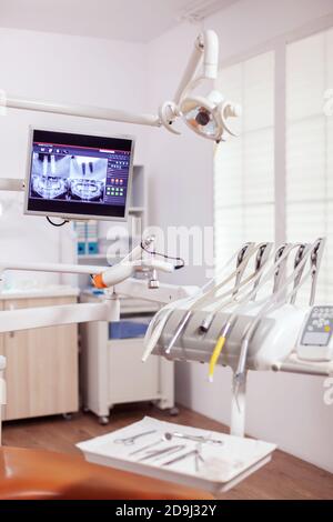 Close-up view of dental tools and professional chair at dentist. Stomatology cabinet with nobody in it and orange equipment for oral treatment. Stock Photo