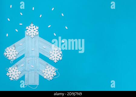 Creative Christmas tree made of medical masks with pills and white snowflakes on a blue background, copy space, top view, close-up. Stock Photo