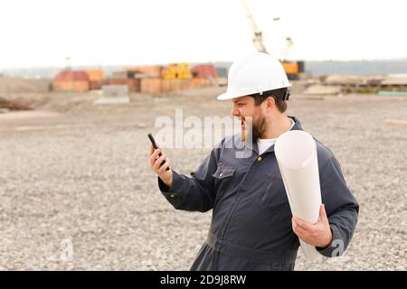 Caucasian building engineer holding VHF walkie talkie and papers on construction site. Stock Photo