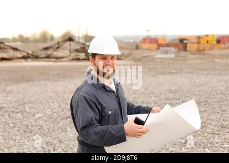 Caucasian foreman holding VHF walkie talkie and papers on construction site. Stock Photo