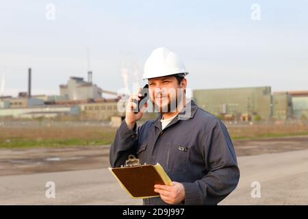 Portrait of foreman talking by walkie talkie on construction site and holding papers. Stock Photo
