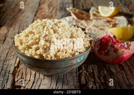 Bowl of healthy organic couscous and quinoa served with fresh pomegranate and flat bread on an old textured cracked wood table Stock Photo