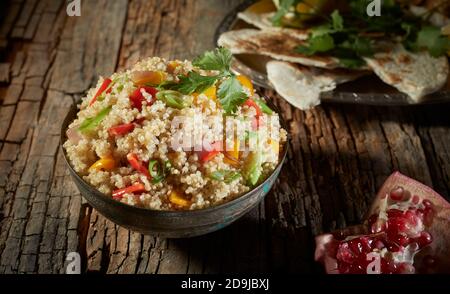 Bowl of mixed quinoa and couscous salad with greens and colorful sweet peppers served on a rustic table with fresh pomegranate in a high angle view Stock Photo