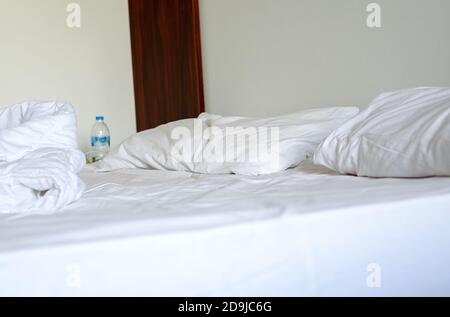 Close-up of white bedding sheets and pillow against the background of a hotel room, unmade bed. Stock Photo