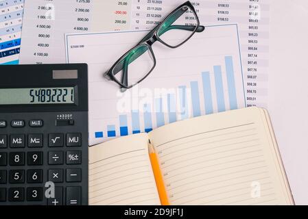 Workplace with financial papers, charts, accounting documents, a large calculator, an open notebook and glasses. Analysis of the company's income and Stock Photo