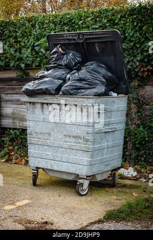 overflowing 1100 litre wheelie bin with the bin lid open outside a shop Stock Photo