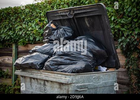 overflowing 1100 litre wheelie bin with the bin lid open outside a shop Stock Photo