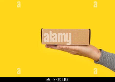 Woman hand holding a cardboard box on a yellow background Stock Photo