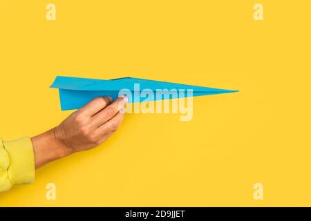 Woman hand holding a blue paper plane on a yellow background Stock Photo