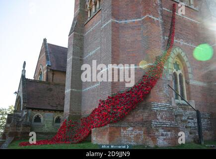 Hand knitted poppies creating 'A Fall of Poppies for the Fallen' hang from the tower of St Michael and All Angels church in Lyndhurst, Hampshire. Stock Photo