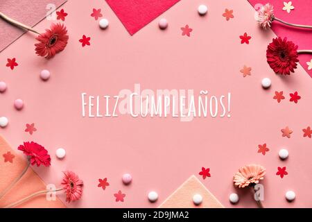 Feliz Cumpleanos means Happy Birthday in Spanish language. Flat lay, gerbera flowers on pink paper Stock Photo