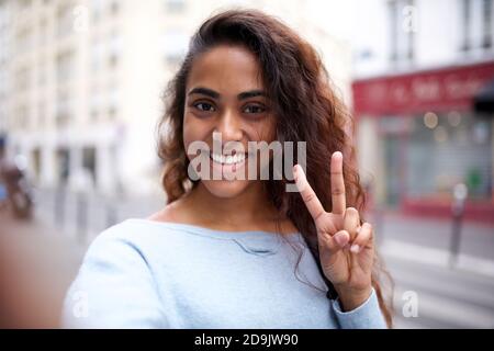 Portrait young Indian woman smiling and taking selfie with peace hand sign Stock Photo