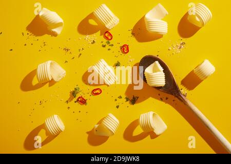 Butter curls and wooden spoon on a bright yellow background with shadows and scattered condiments and chili peppers viewed as a flat lay in a food sty Stock Photo