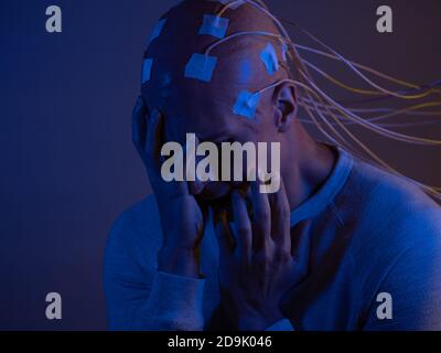 Man with a bald head with wires connected. Fear and anxiety. Examination of the brain, mind control. Stock Photo