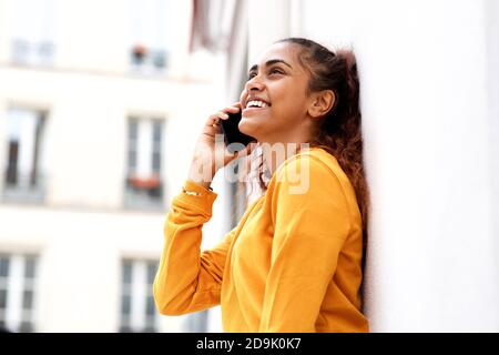 Close up side portrait happy young woman leaning against white wall talking with mobile phone Stock Photo