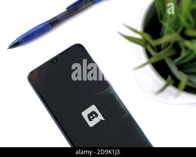 Lod, Israel - July 8, 2020: Modern minimalist office workspace with black mobile smartphone with Discord app launch screen with logo on white backgrou Stock Photo