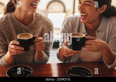 Two females sitting at a coffee table talking and laughing. Happy woman friends in a cafe having coffee. Stock Photo