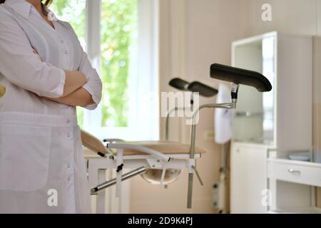 Closeup of a doctor in white uniform, with the left side. Stands in a half turn to the gynecological chair.  Stock Photo