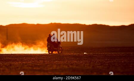 On a motorcycle in the Gobi desert. Dust from under the wheels. Wild Mongolian road. Stock Photo