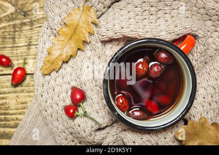 Cup of tea with rose hips, warm clothes and dried leaves on rustic wooden background, top view, close-up. Autumn concept. Stock Photo