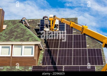 Workers installing solar panels on private home hexagonal roof felt on sunny day, blue sky. Real life. Home power plant. Stock Photo