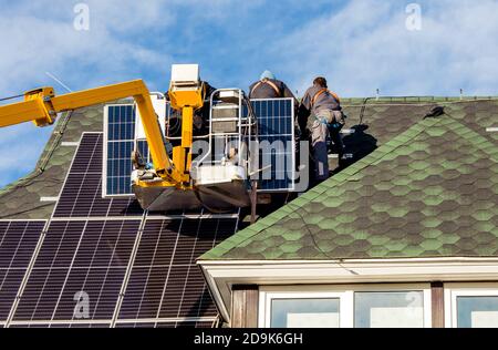 Workers installing solar panels on private home hexagonal roof felt on sunny day, blue sky. Real life. Home power plant. Stock Photo