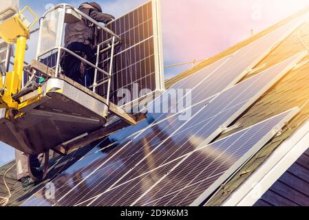 Workers installing solar panels on private home hexagonal roof felt on sunny day, blue sky. Real life. Home power plant. Stock Photo