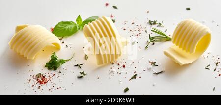 Three stylish ridged butter curls or shavings with scattered fresh rosemary, parsley and basil with spices on white in a panorama banner in a food sty Stock Photo