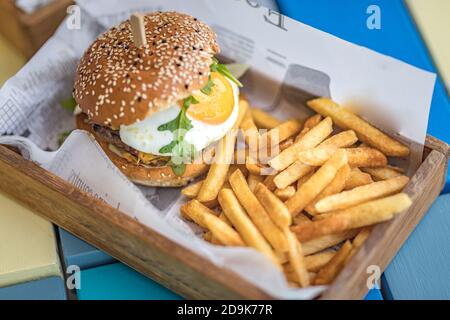 Hamburger and fries. Giant burger with french fries in wooden bowl plate. Gourmet homemade hamburger in outdoor restaurant table top Stock Photo