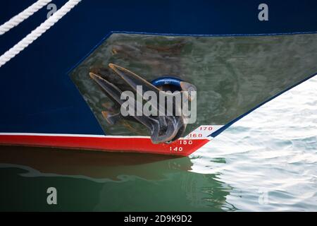 Red anchor on blue vessel. The ship's anchor is in the raised position. Stock Photo