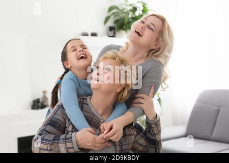 Three generations of women. Beautiful woman and teenage girl are kissing their granny while sitting on couch at home Stock Photo