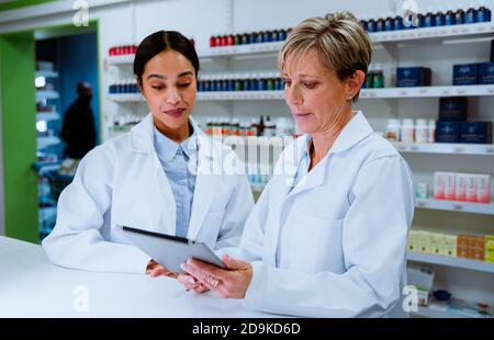 Caucasian pharmacist manager helping mixed race assistant using digital tablet standing in pharmacy drugstore Stock Photo