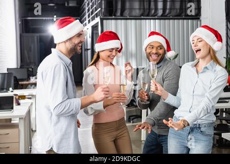 Cheerful multiethnic businesspeople in santa hats having fun with glasses of champagne in office Stock Photo