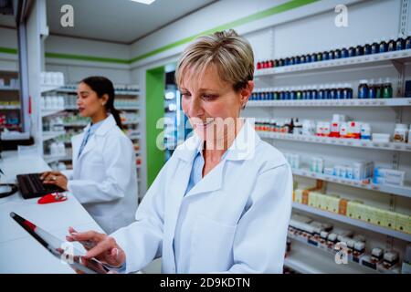 Senior caucasian pharmacist scrolling on digital tablet locating medication in drugstore Stock Photo