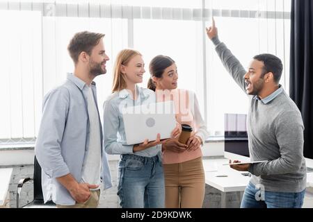 Excited indian businessman having idea while holding digital tablet near colleagues with laptop Stock Photo