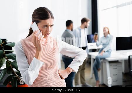 Angry businesswoman talking on smartphone with colleagues on blurred background Stock Photo