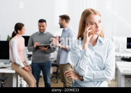 Pensive businesswoman standing near colleagues working on blurred background Stock Photo