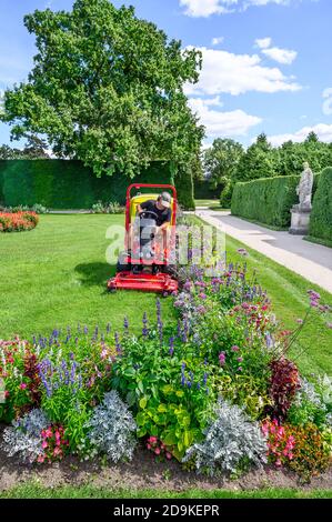 Man mows the grass in flower garden of Lednice chateau by riding mowing machine in sunny day Stock Photo