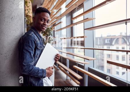 Young positive african american guy standing indoors with laptop in hands Stock Photo