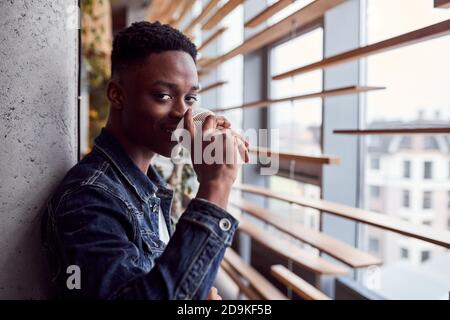 Young positive african american guy standing indoors and drinking coffee Stock Photo