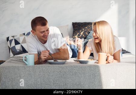 Young lovely couple have a breakfast at home while lying down on bed Stock Photo