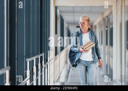 Male young student in jeans clothes is in corridor of a college with books in hands Stock Photo