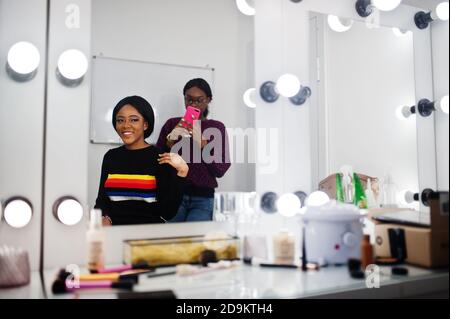 African American woman applying make-up by make-up artist at beauty saloon. Artist make photo on mobile phone of her work. Stock Photo