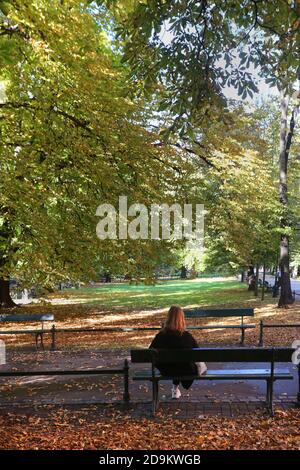 Cracow. Krakow. Poland. Young redhead woman sitting on the park bench looking at autumn trees. Stock Photo