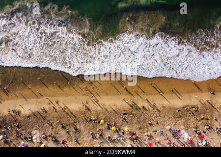 Bird's eye view of crowded beach with bathing people. People relaxing on the beach near ocean unedr umbrellas on sunny day. Aerial view of Playa  Cale Stock Photo
