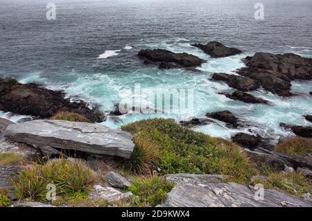 Rocky coast view with waves crash rocks view from above from cape with lush green foliage. Rainy day and foggy overcast sky. Pacific Coast, Bahia Mans Stock Photo