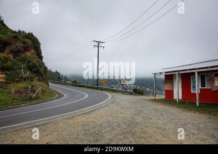 Maicolpue, Osorno, Chile -  February, 2020: Empty curved road with speed limit sign and small closed shop with foggy overcast weather on Pacific Coast Stock Photo