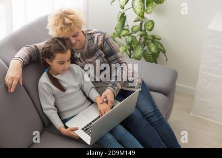 Smart little girl grandchild sit on couch shopping online with excited senior grandmother, teen granddaughter and smiling granny buy on internet Stock Photo