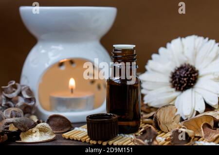 Aroma lamp with a burning candle, a bottle of aromatic oil, in brown tones, decorated with a flower. Relaxation and spa atmosphere. Aromatherapy Stock Photo